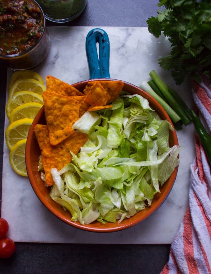 A bowl with a base of lots of lettuce and a few tortilla chips ready for layering the chicken fajita 