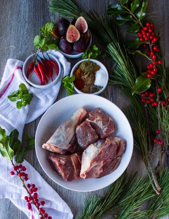 Ingredients for cooking lamb: lamb shoulder pieces cut up surrounded by a bowl of Moroccan spice, surrounded by red chillies, fresh figs and a tea towel 