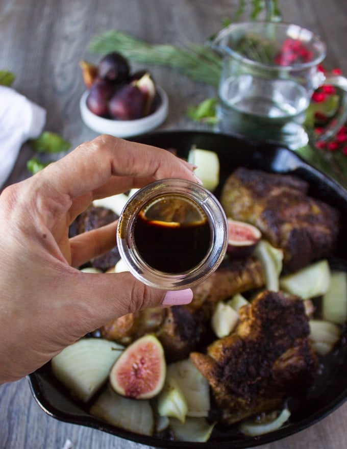 A hand holding sweet balsamic vinegar to be added to the lamb skillet for cooking lamb in a sweet spicy sauce