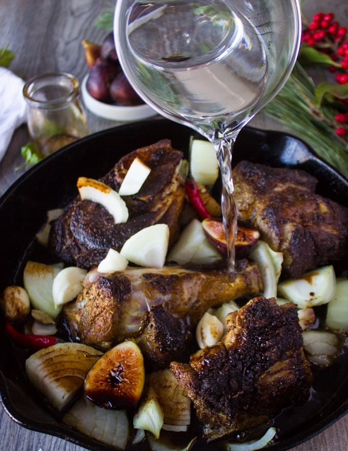 Water being poured over the lamb meat in a skillet with all the sweet and spice sauce ingredients ready to roast