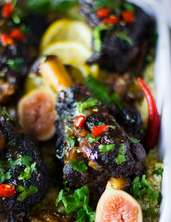 Cooked lamb surrounded by lemon slices, fresh figs and red chillies on a plate of couscous