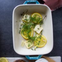 Baking dish layered with butter, lemon slices, garlic, fresh herbs and ready for the fish