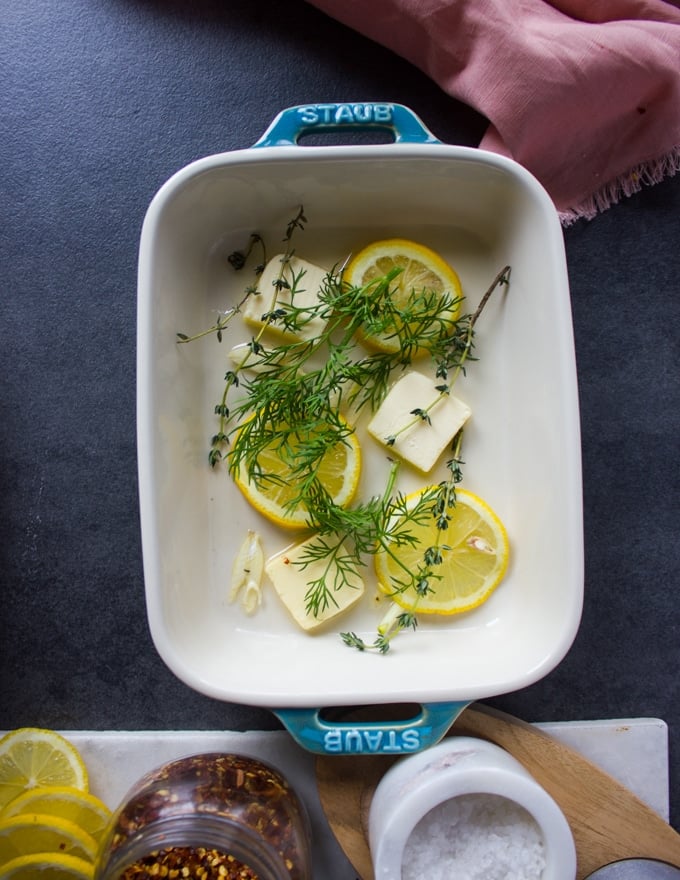 Baking dish layered with butter, lemon slices, garlic, fresh herbs and ready for the fish