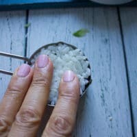 A hand pressing down the sushi rice as the final layer for the crab sushi and pressing it down firmly