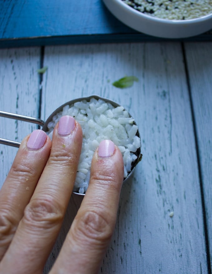 A hand pressing down the sushi rice as the final layer for the california roll and pressing it down firmly to finish the sushi stack