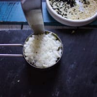 A hand running a knife around the sushi stack to release the crab sushi from the measuring cup