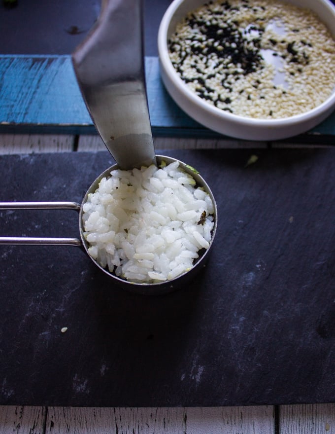 A hand running a knife around the sushi stack to release the crab sushi from the measuring cup