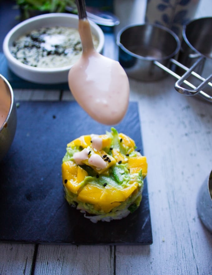 A spoon drizzling some spicy mayo over crab sushi