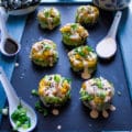 A selection of 8 crab sushi made into sushi sacks over a black board surrounded by a spoon of spicy mayo and a spoon of scallions and soy sauce