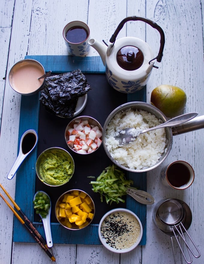 Ingredients for the crab sushi and sushi stacks, a pot of rice, seaweed sheets, spicy mayo, soy sauce, crab meat, mashed avocado, mango, scallions, shredded cucumbers, sesame seeds, dry measuring cups 