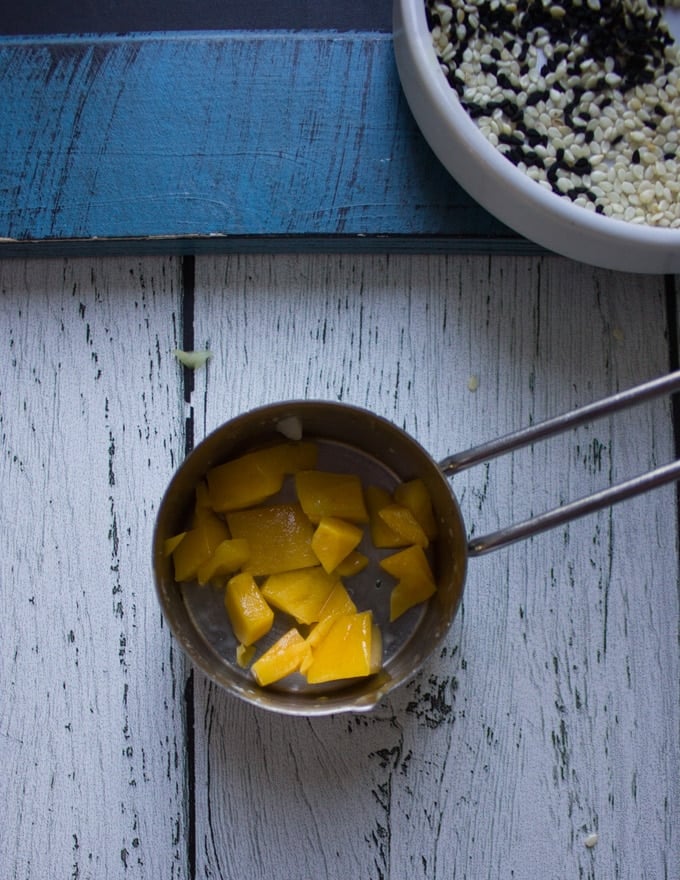 A measuring cup , the 1/3 cup measuring cup with mango chunks at the bottom 