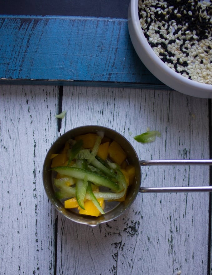 shredded cucumbers added over the mango chunks in the same measuring cups layering the sushi stacks 