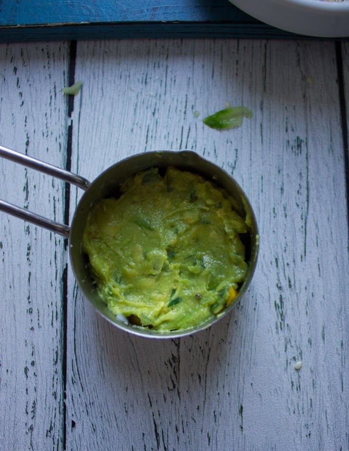 A layer of mashed avocados goes over the avocados and mangoes in the same measuring cup