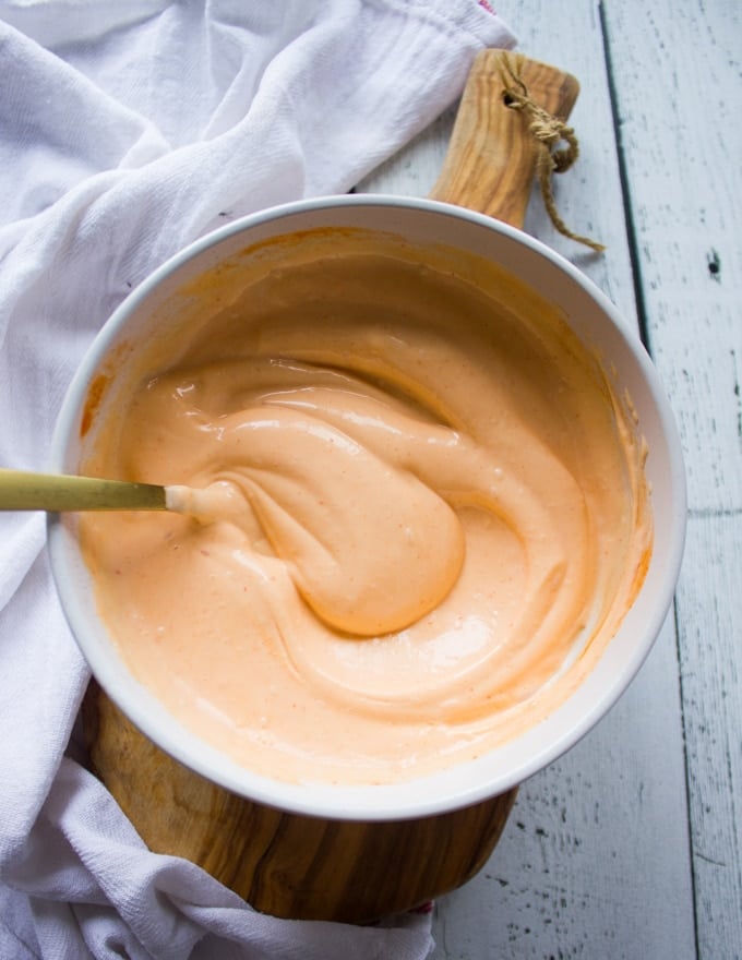 A bowl of spicy mayo recipe and a spoon swirled in to show the texture and creamy sauce