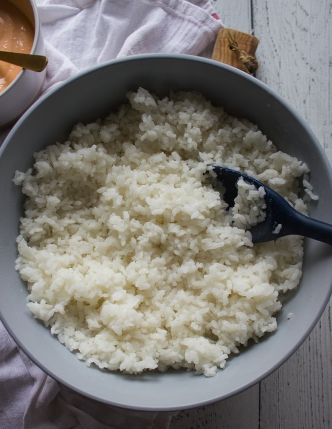 perfect sushi rice cooked and cooled down ready to use in a large blue bowl and a spoon inside