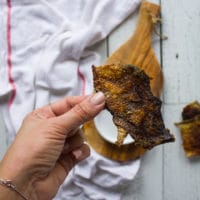 A hand holding a piece of crispy salmon skin for sprinkling over the sushi burrito