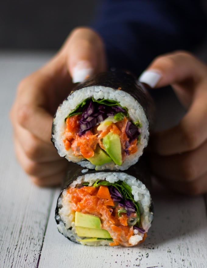 two hands trying to hold one sushi burrito sliced in half over a white board