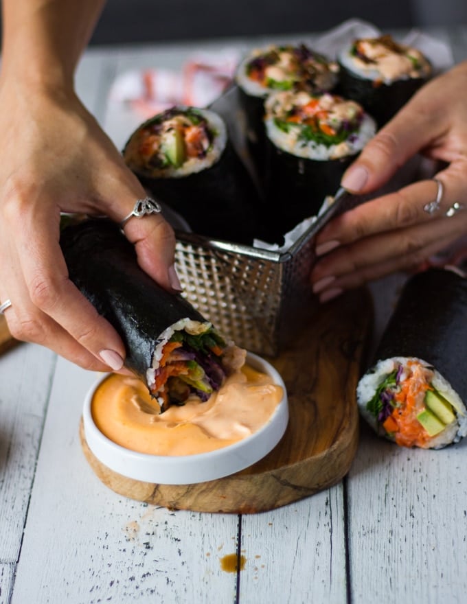 A hand dipping a sushi burrito into more spicy mayo