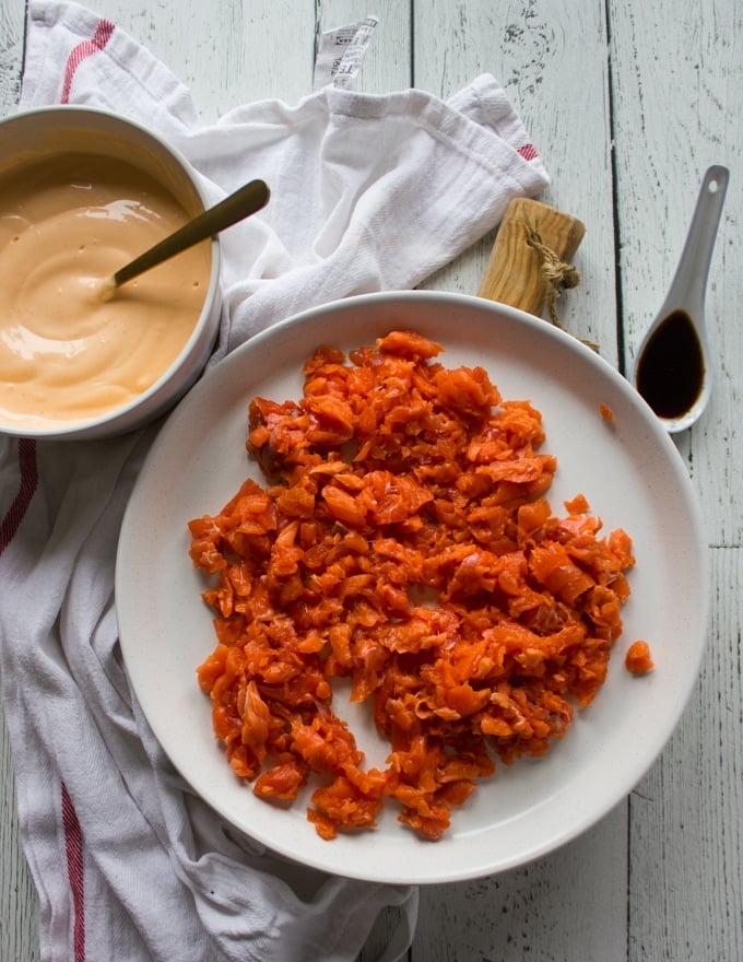 Ingredients for spicy salmon sushi including a plate of raw chopped salmon, a bowl of spicy mayo and a teaspoon of soy sauce