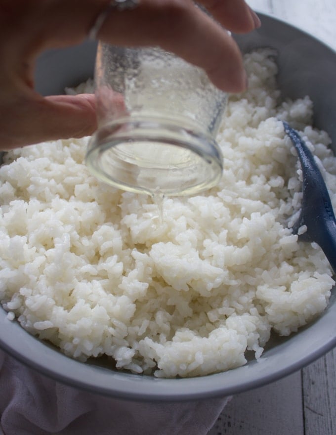 A hand pouring the seasoning from the bowl into the cooled sushi rice to flavor it