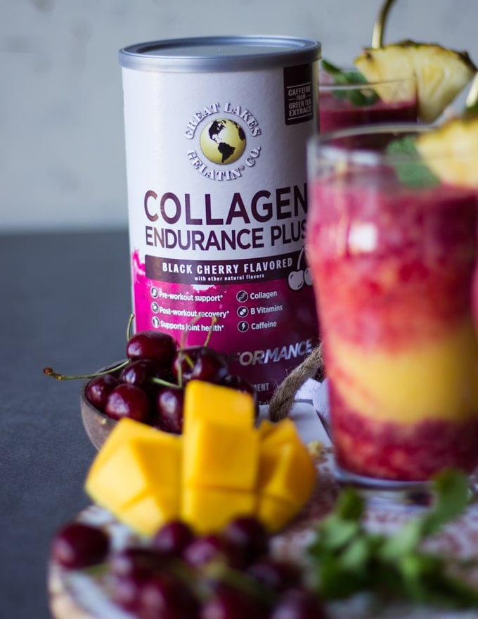 A box of collagen to thicken the smoothies and a hazy cup of tropical smoothie and some tropical fruits and fresh mint on a wooden board