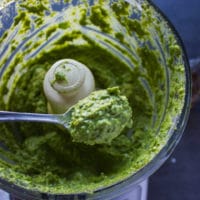 A spoon holding off a the poblano sauce in the food processor showing how smooth and creamy and ready the sauce is