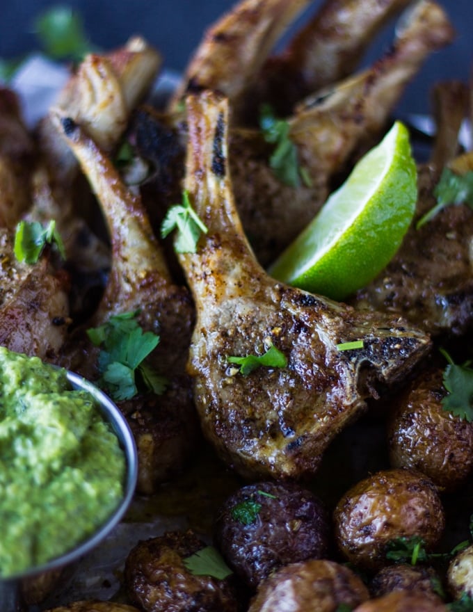 A pile of lamb chops perfectly cooked in the air fryer with lime wedges and cilantro showing the texture of crisp outside of the lamb