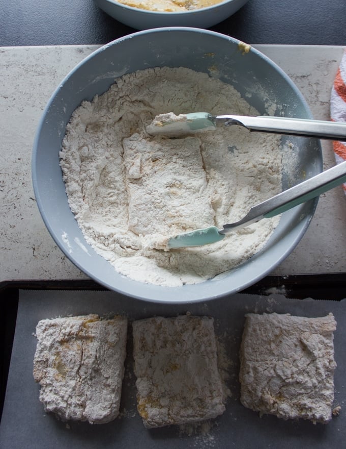 The fish fillets being dredged once again in the flour bowl and a tong is used to coat it