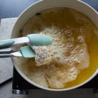 A tong placing the fish in the bubbling oil for the fish fry to start frying