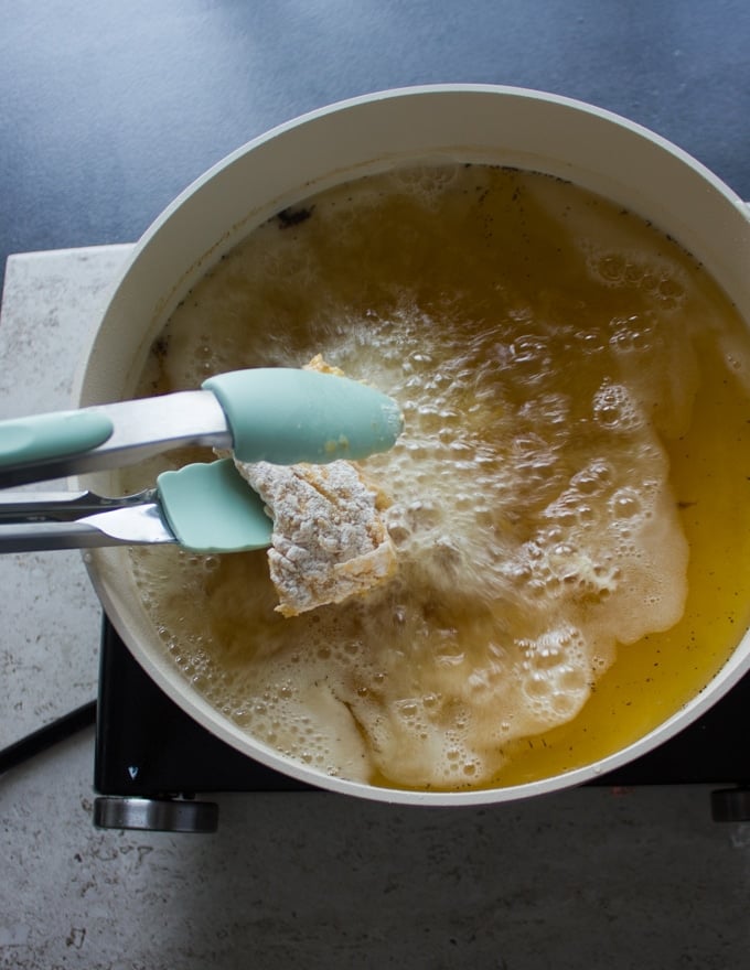 A tong placing the fish in the bubbling oil for the fish fry to start frying 