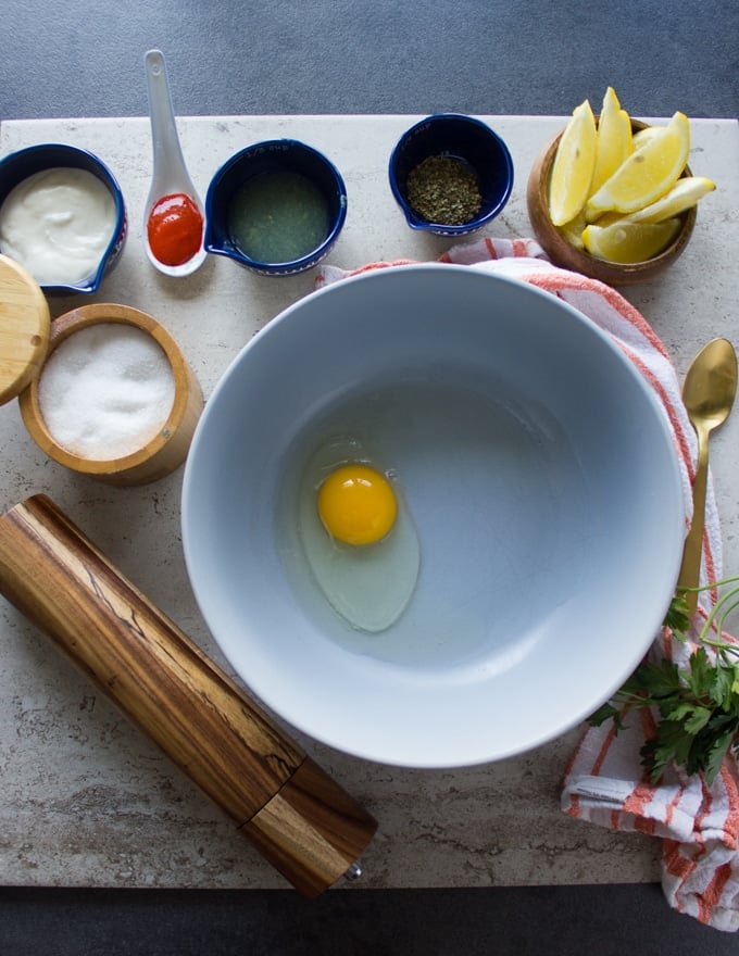 The wet seasoning bowl for fish fry seasoning including a bowl of egg, lemon juice, spices like salt, oregano and pepper, hot sauce, garlic mayo