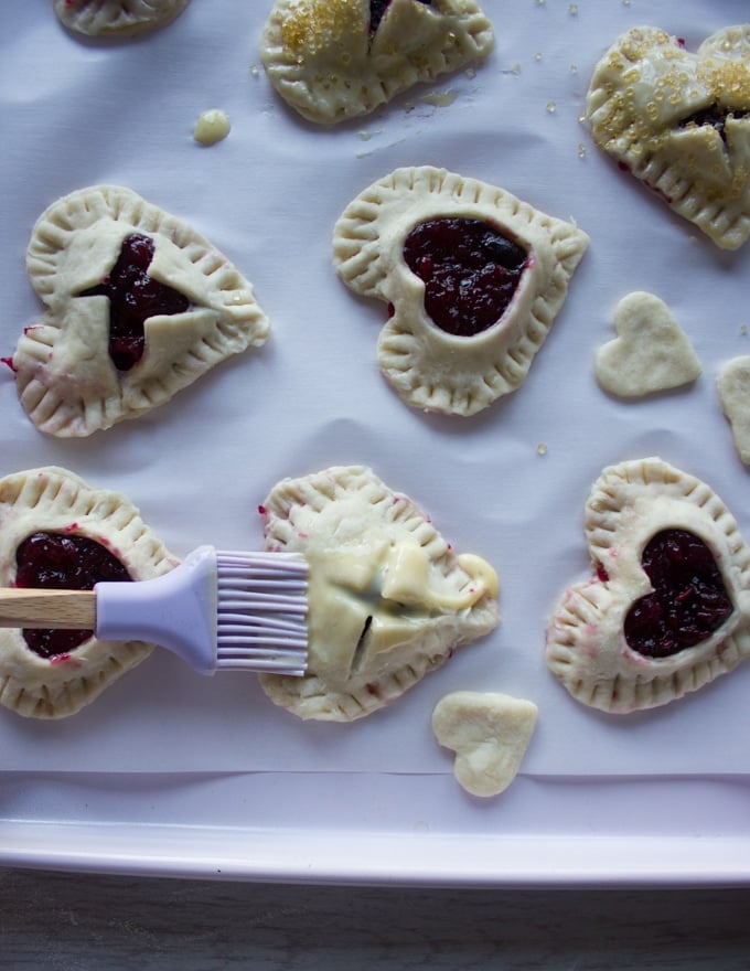 A pastry brush brushing the egg wash over the tops of the cherry pies