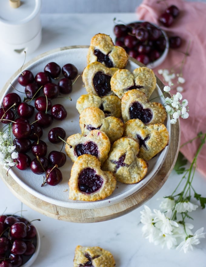 Top view of the plate of sweet cherry pies on a side and fresh cherries on the other side. 