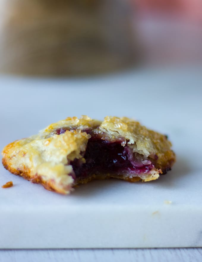 A sweet cherry pie on a white marble bitten up to show the inside flakey pie dough and pink cherry filling 