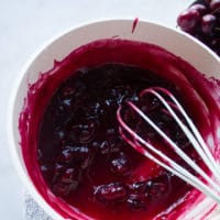 A pot with the cherry pie filling cooked and ready with a whisk in the pan