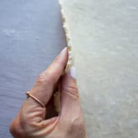 A hand holding a rolled out pie crust showing the thickness of the dough needed t make the cherry pie