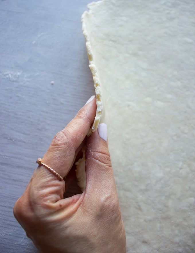 A hand holding a rolled out pie crust showing the thickness of the dough needed t make the cherry pie