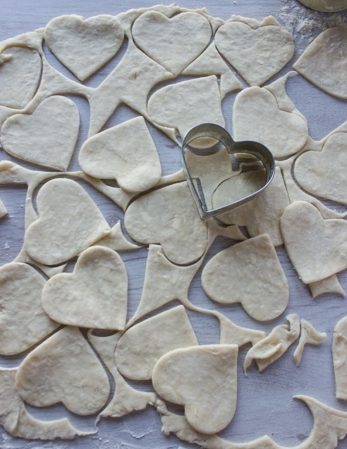 a heart cookie cutter cutting out the pie dough into small pies