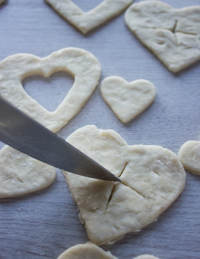 A knife cutting slits on the tops crusts of the mini cherry pies