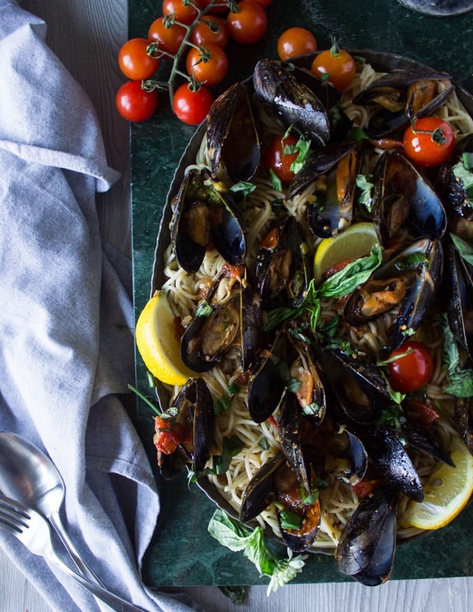 A huge plate of mussels marinara on a green marble ad pasta for mussels pasta and fresh basil