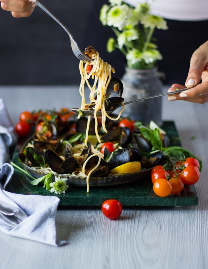 two hands serving the mussels pasta with the mussels marinara over a plate of mussels marinara 