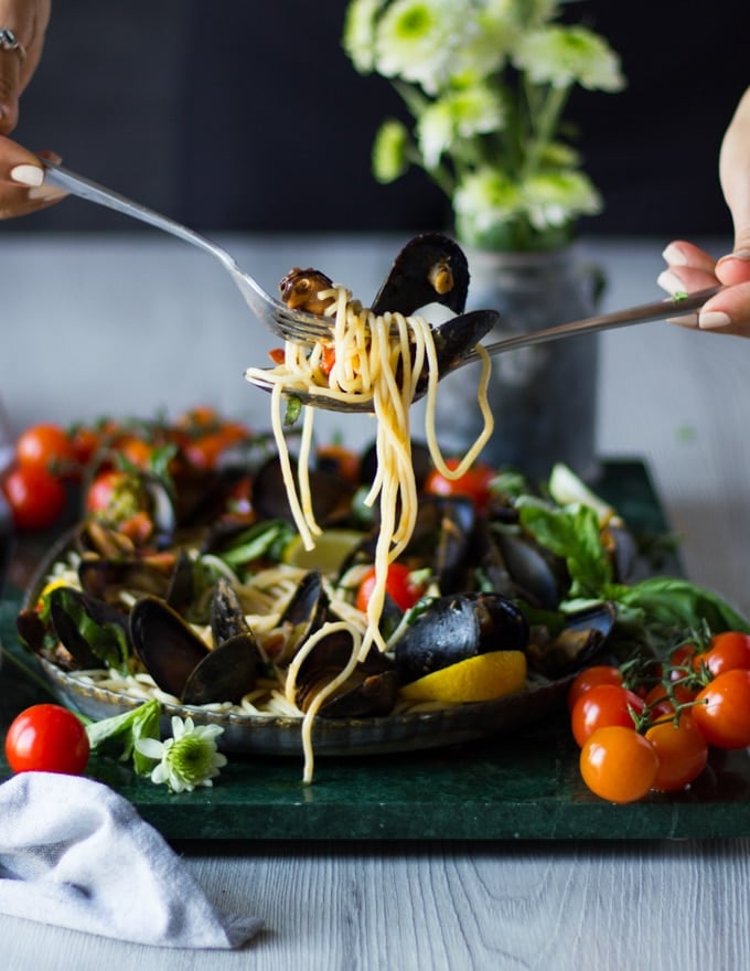 two hands with spoons and forks holding off pasta from a plate with mussels marinara and mussel pasta