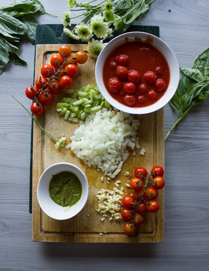 Ingredients for mussels marinara including chopped onions, celery, garlic, basil pesto and canned tomatoes on a cutting board