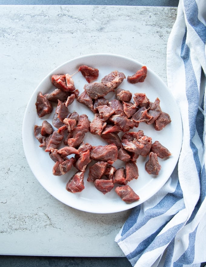 Beef tips on a white plate on a marble with a tea towel showing the cut of meat