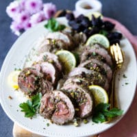 A plate of boneless leg of lamb recipe served with lemon slices and extra pistachios on top