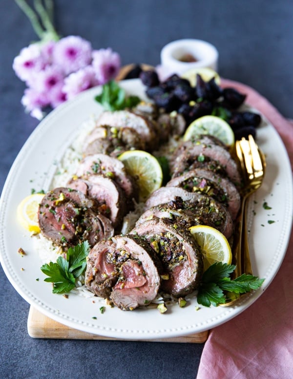 A plate of boneless leg of lamb recipe served with lemon slices and extra pistachios on top