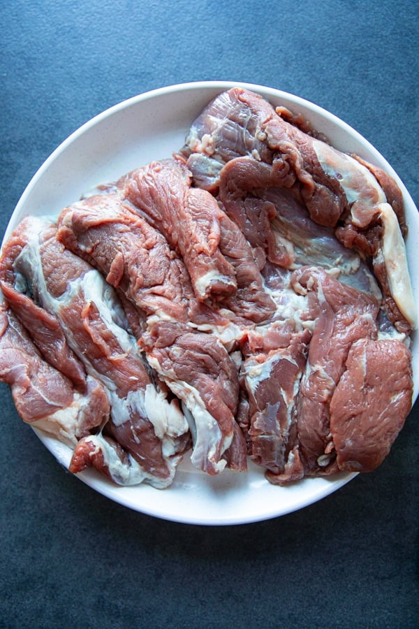 a piece of boneless leg of lamb raw on a plate. Trimmed and ready for the recipe.