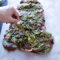 A hand holding a spoon and spreading the filling over the boneless leg of lamb