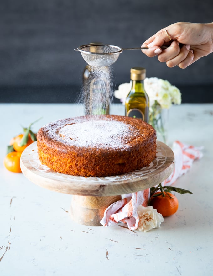 A hand dusting some confectioner's sugar right over the cake for a final finish