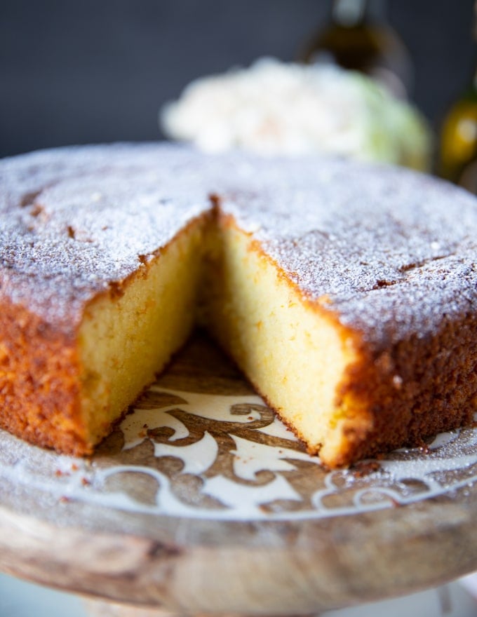 A close up of an olive oil cake with one slice removed on a serving olate showing the inside of the olive oil cake texture 